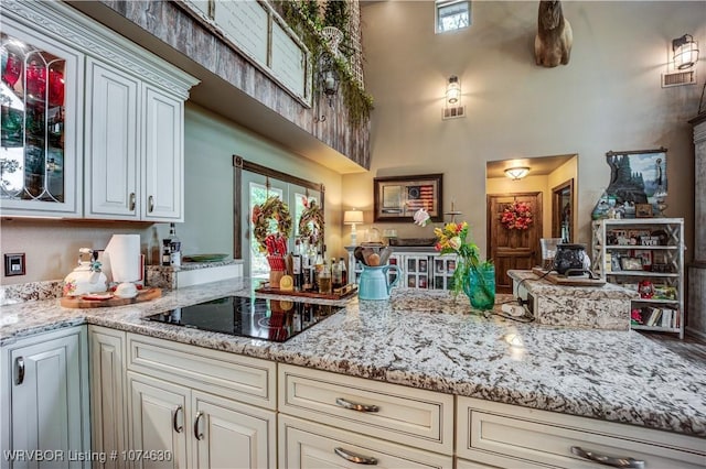 kitchen featuring black electric stovetop, light stone counters, and a high ceiling