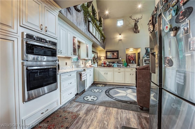 kitchen with kitchen peninsula, light stone counters, stainless steel appliances, sink, and hardwood / wood-style floors