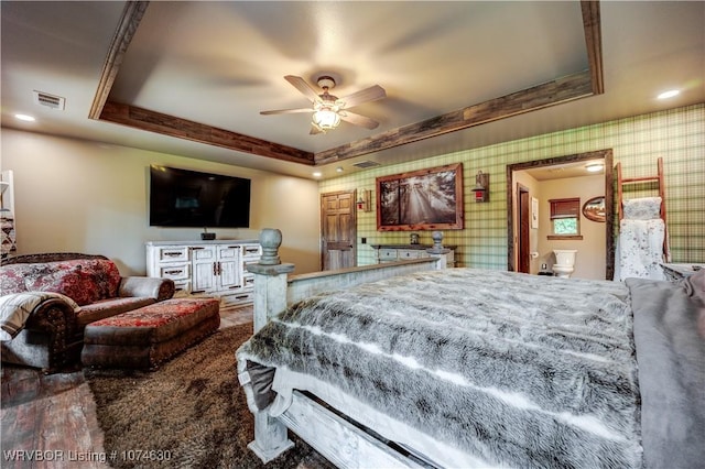 bedroom with ceiling fan, a raised ceiling, and ensuite bath