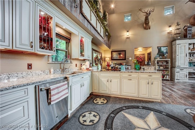 kitchen featuring light stone countertops, sink, a high ceiling, stainless steel dishwasher, and kitchen peninsula