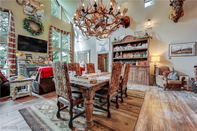 dining space with hardwood / wood-style floors, a notable chandelier, a stone fireplace, and a towering ceiling