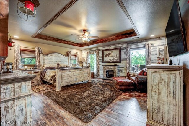 bedroom featuring a tray ceiling, a stone fireplace, and wood-type flooring