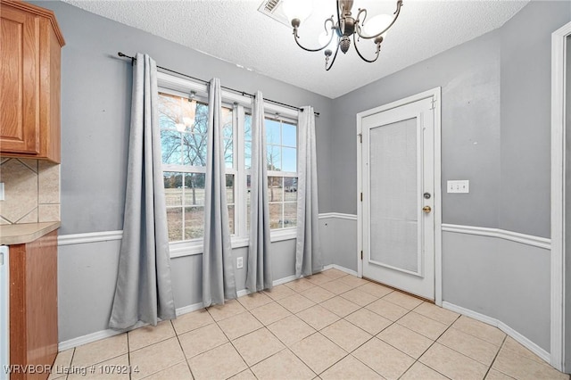 entryway featuring a textured ceiling, light tile patterned flooring, baseboards, and a notable chandelier