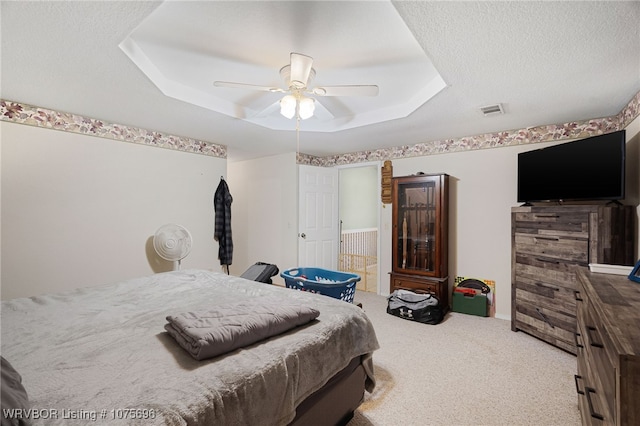 carpeted bedroom featuring a tray ceiling, ceiling fan, and a textured ceiling