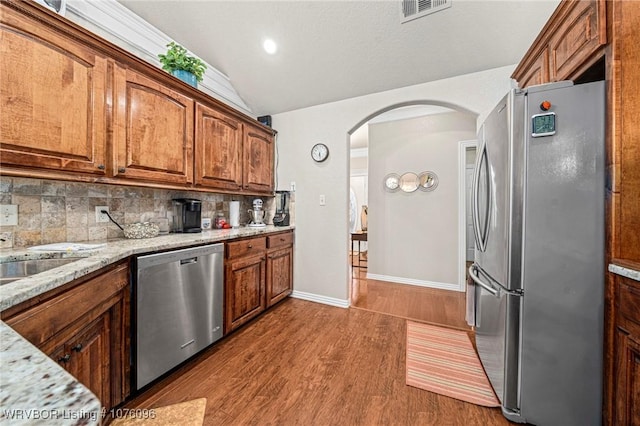 kitchen with decorative backsplash, light stone counters, lofted ceiling, and appliances with stainless steel finishes