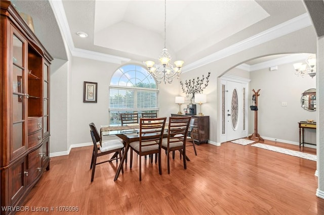 dining space featuring wood-type flooring, a raised ceiling, ornamental molding, and a notable chandelier