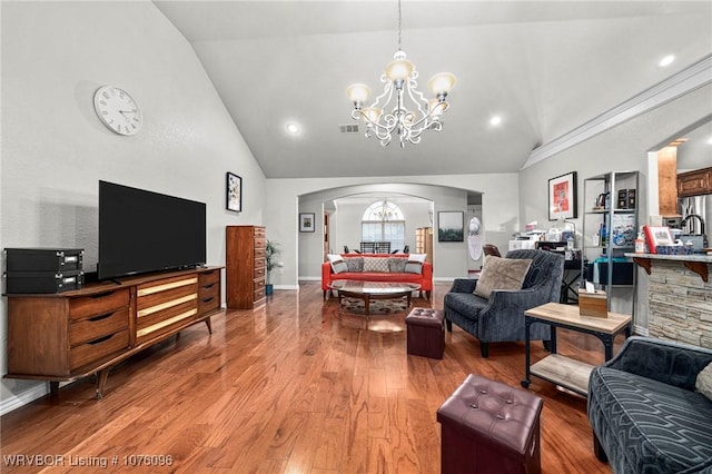 living room featuring hardwood / wood-style flooring, vaulted ceiling, a notable chandelier, and crown molding