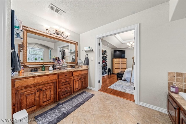 bathroom with a textured ceiling, vanity, an inviting chandelier, and tile patterned floors