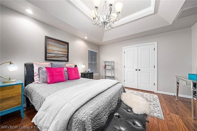 bedroom featuring ornamental molding, a raised ceiling, dark wood-type flooring, a chandelier, and a closet