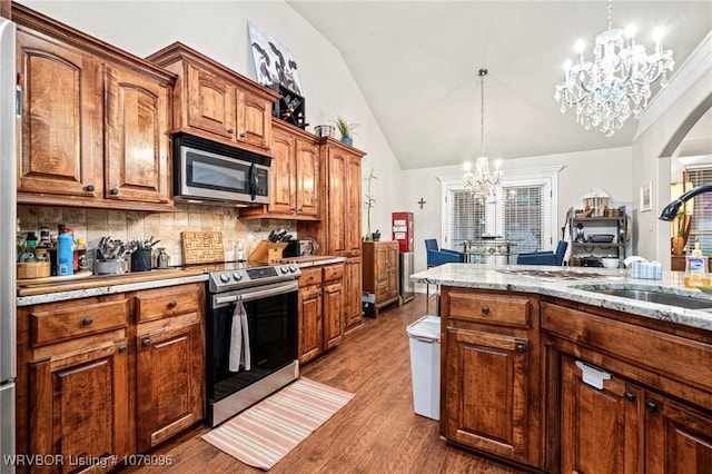 kitchen with decorative backsplash, appliances with stainless steel finishes, sink, hardwood / wood-style flooring, and an inviting chandelier