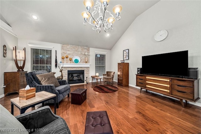 living room featuring a stone fireplace, hardwood / wood-style floors, vaulted ceiling, and a notable chandelier