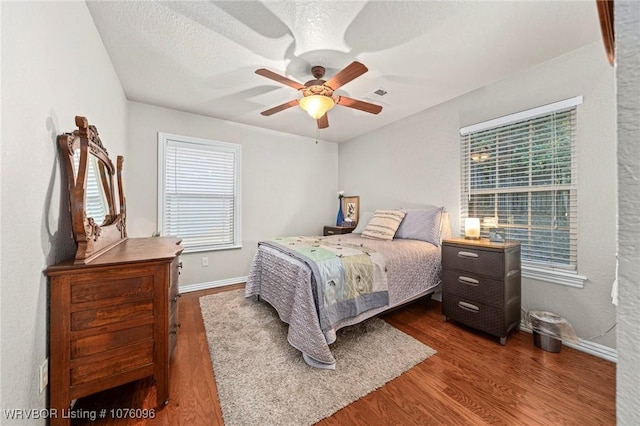 bedroom with a textured ceiling, ceiling fan, and dark wood-type flooring