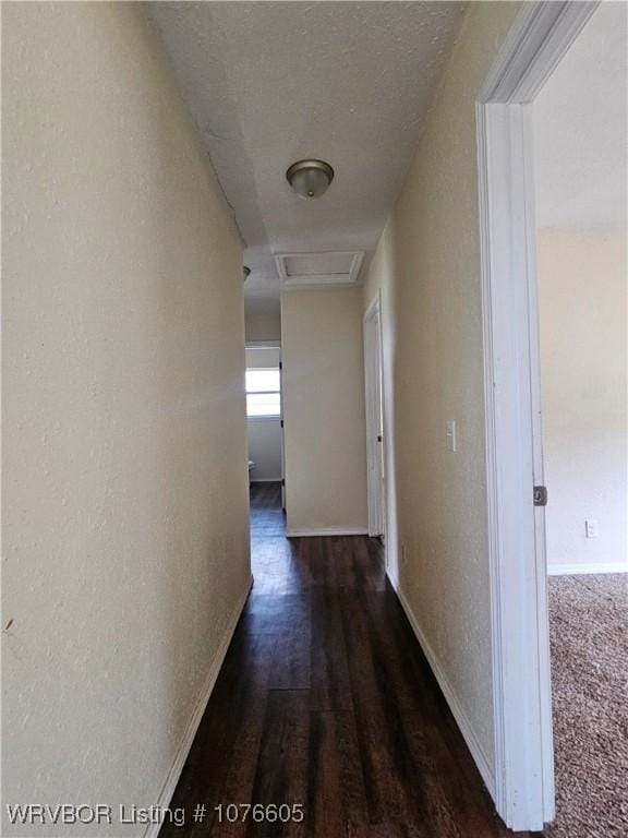 hall featuring dark colored carpet and a textured ceiling