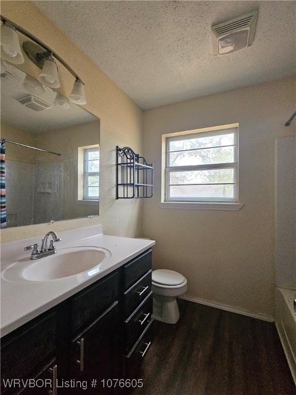 full bathroom with shower / tub combo, vanity, a textured ceiling, hardwood / wood-style floors, and toilet