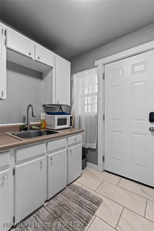 2101 Birnie Ave, Fort Smith, AR 72904 - kitchen featuring white microwave, a sink, a textured ceiling, and white cabinetry