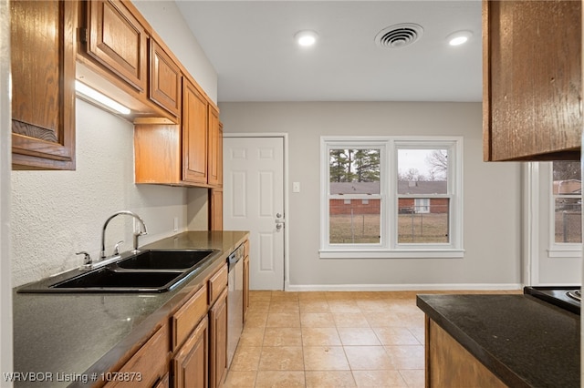 kitchen featuring dark stone countertops, sink, light tile patterned floors, and stainless steel dishwasher