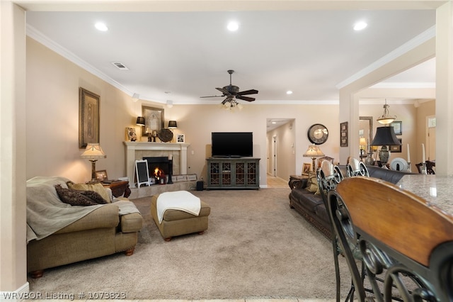 carpeted living room featuring ceiling fan, crown molding, and a tiled fireplace