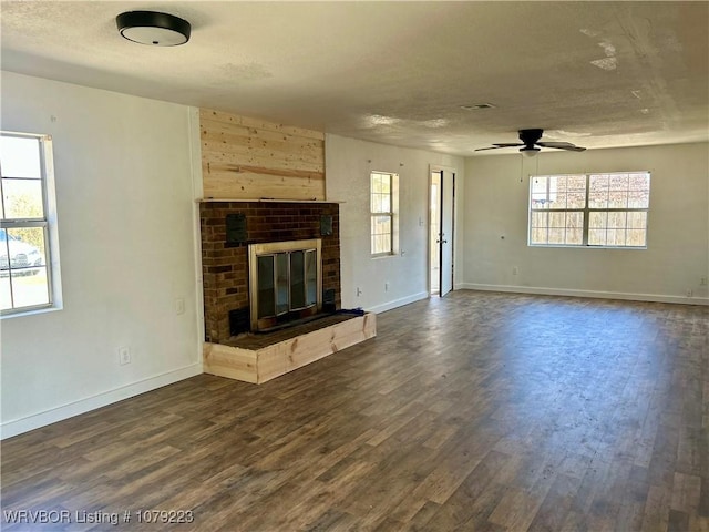 unfurnished living room featuring dark wood-type flooring, a brick fireplace, visible vents, and baseboards