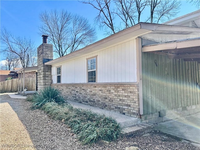 view of property exterior featuring a chimney, fence, and brick siding