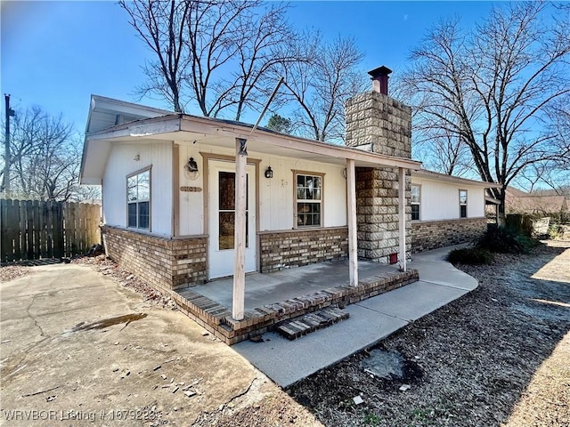 view of front facade with a chimney, fence, a porch, and brick siding