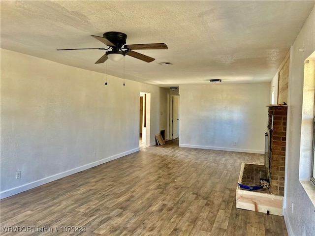 unfurnished room featuring a brick fireplace, ceiling fan, a textured ceiling, wood finished floors, and baseboards