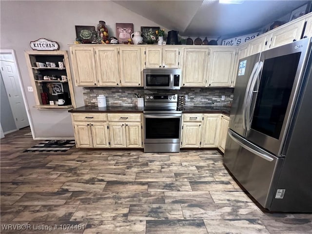 kitchen with tasteful backsplash, cream cabinets, stainless steel appliances, and lofted ceiling