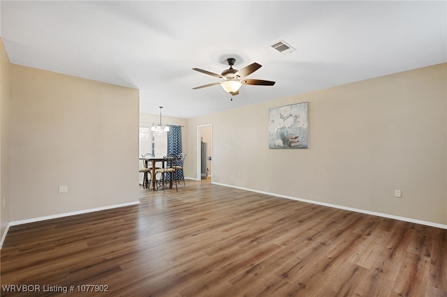 spare room with wood-type flooring and ceiling fan with notable chandelier