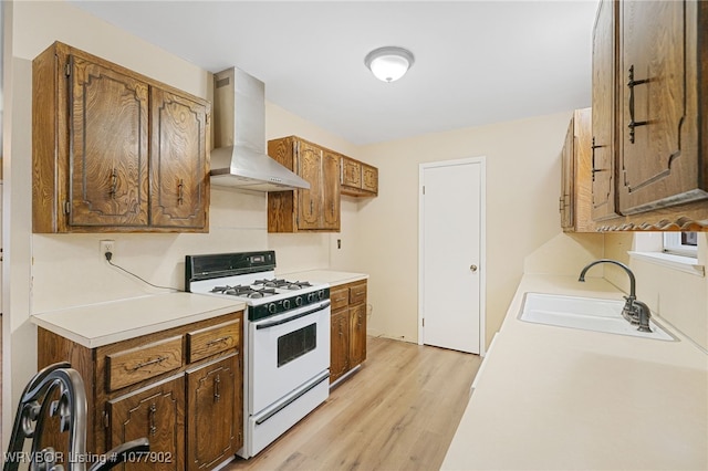 kitchen featuring light wood-type flooring, sink, white range with gas cooktop, and wall chimney range hood