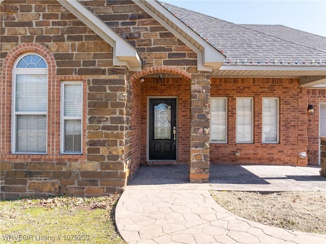 entrance to property featuring stone siding, a shingled roof, and brick siding