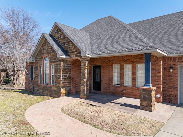 view of front of house with stone siding, a front lawn, roof with shingles, and brick siding