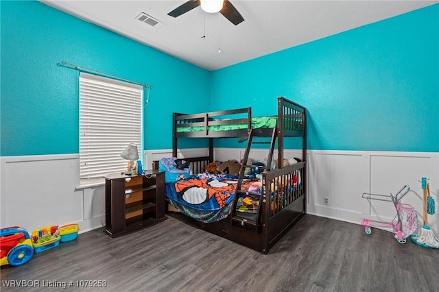 bedroom with wainscoting, visible vents, ceiling fan, and wood finished floors