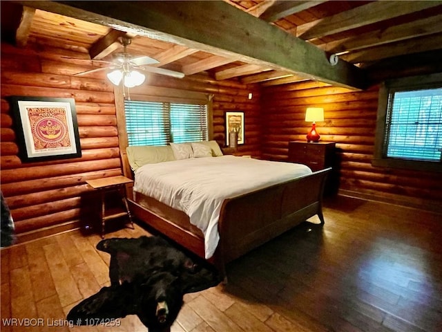 bedroom with beamed ceiling, ceiling fan, rustic walls, and hardwood / wood-style flooring