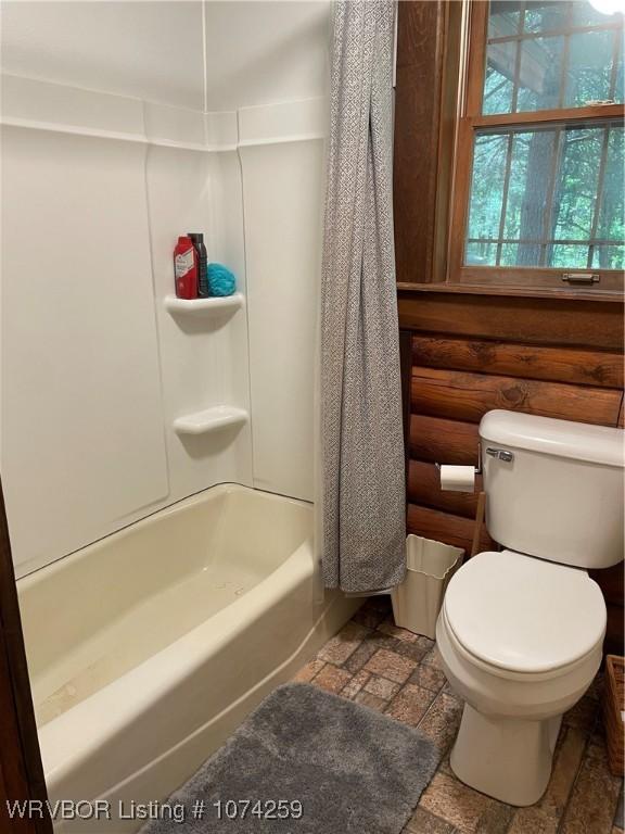 bathroom with shower / bathtub combination with curtain, log walls, and toilet