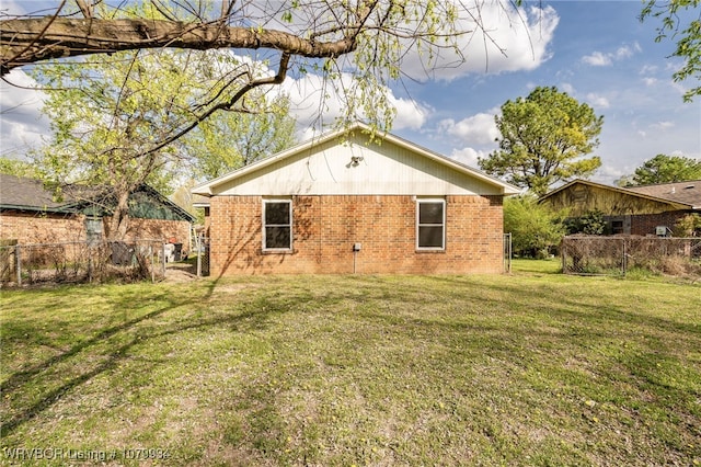 rear view of house featuring a lawn, brick siding, and fence