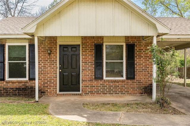 doorway to property with brick siding, a shingled roof, and a carport