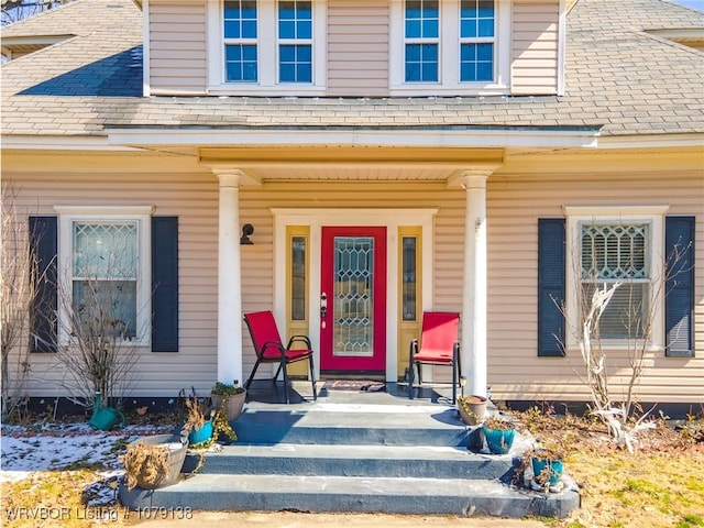 doorway to property with a shingled roof and a porch