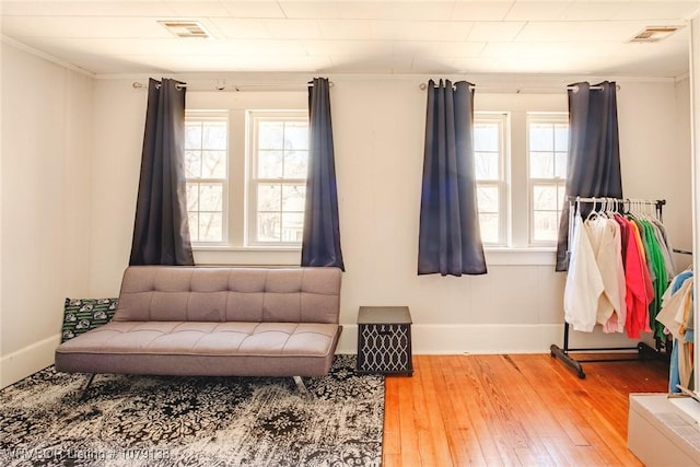 interior space with baseboards, visible vents, wood finished floors, and ornamental molding