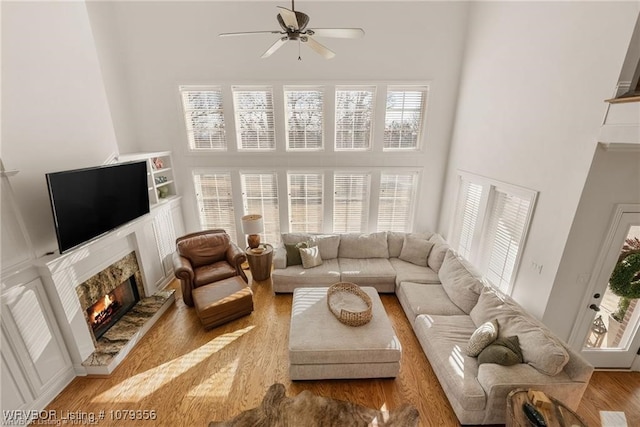 living area featuring a high ceiling, a ceiling fan, a fireplace, and wood finished floors