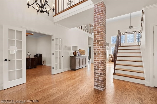 stairway featuring french doors, a towering ceiling, wood finished floors, baseboards, and ceiling fan with notable chandelier