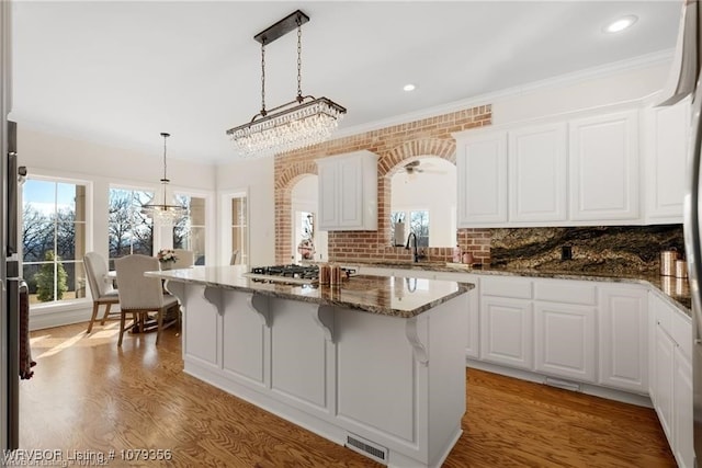 kitchen featuring visible vents, light wood-style floors, white cabinetry, a kitchen island, and a kitchen bar