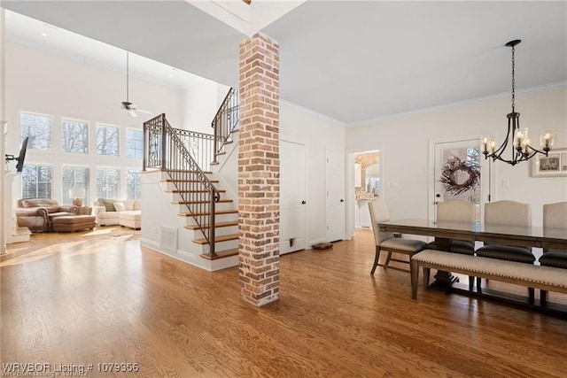 dining room featuring ceiling fan with notable chandelier, a high ceiling, wood finished floors, stairs, and ornamental molding