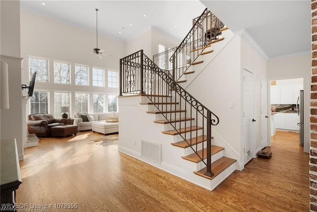 staircase with ornamental molding, wood finished floors, and visible vents