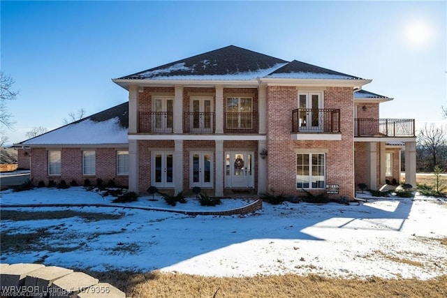 snow covered property featuring brick siding, french doors, and a balcony