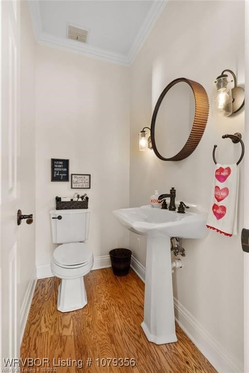 half bathroom with baseboards, visible vents, toilet, ornamental molding, and wood finished floors