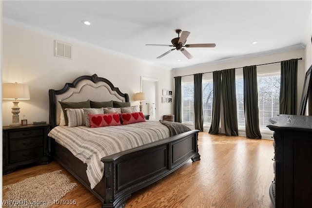 bedroom with light wood finished floors, visible vents, and crown molding