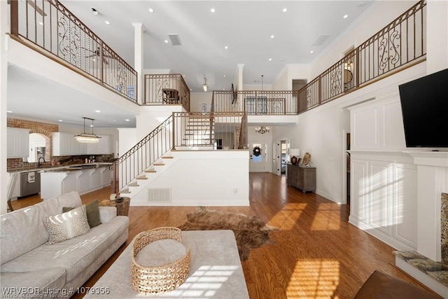 living room with light wood-type flooring, stairs, visible vents, and a towering ceiling