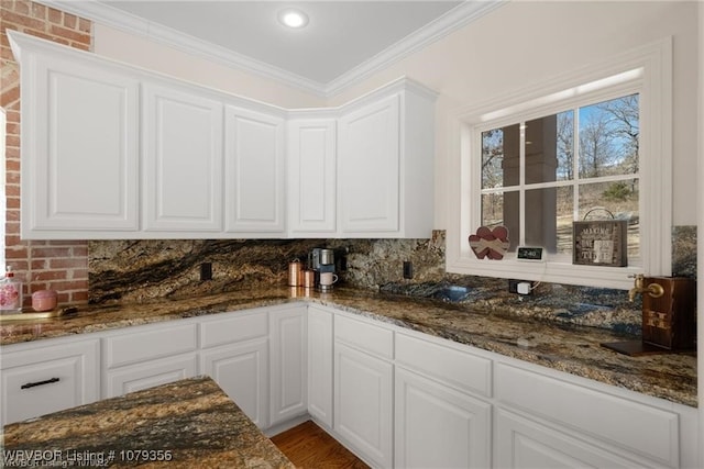 kitchen featuring crown molding, dark stone counters, and white cabinets