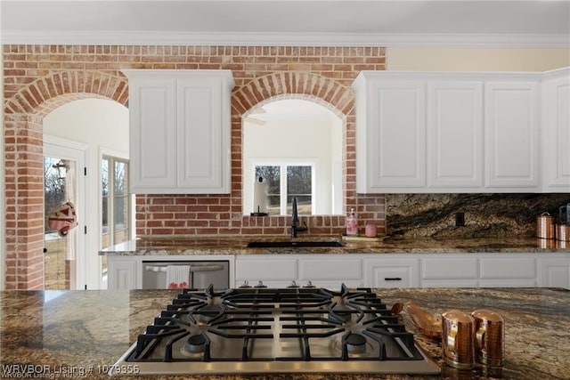 kitchen featuring arched walkways, stainless steel appliances, a sink, white cabinets, and dark stone countertops