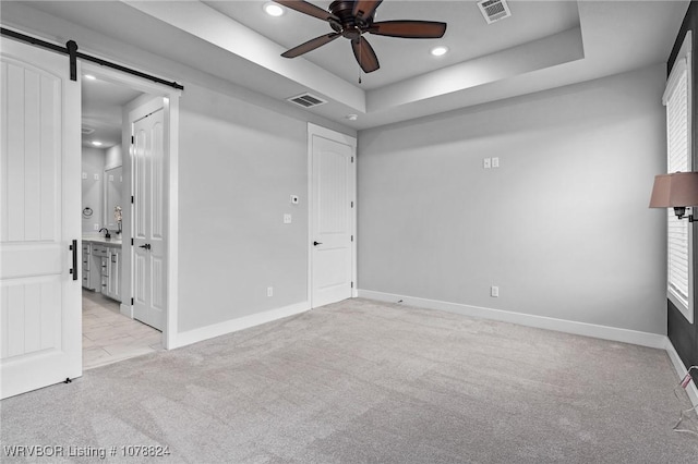 carpeted spare room featuring a healthy amount of sunlight, a raised ceiling, ceiling fan, and a barn door