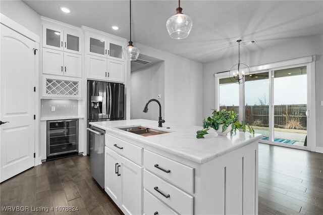 kitchen featuring sink, hanging light fixtures, stainless steel appliances, an island with sink, and white cabinets